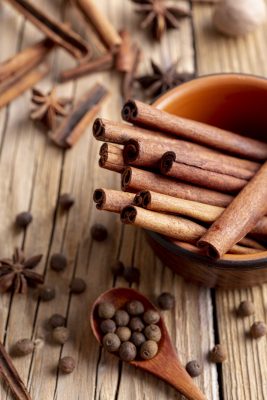 Close-up of rolled cinnamon sticks in a bowl, with star anise and allspice berries on a rustic wooden background.