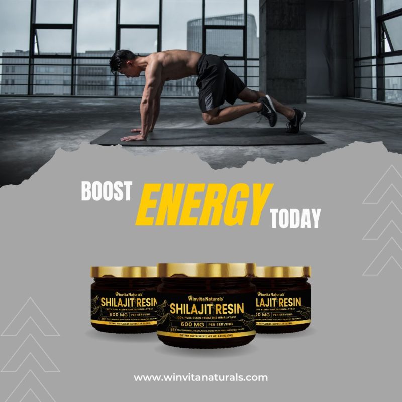 An advertisement image featuring two jars of Shilajit resin supplements from Winvita Naturals, each with a potency of 600 mg per serving. The backdrop is a gym setting where a man is doing a dynamic exercise to convey activity and energy. The top section of the image contains a prominent call-to-action in bold, capital letters saying "BOOST ENERGY TODAY", directing viewers' attention to the purported benefits of the product. The website "www.winvitanaturals.com" is advertised at the bottom, suggesting where consumers can learn more or purchase the product. The overall design uses a dark color scheme with yellow highlights to emphasize vitality and vigor.